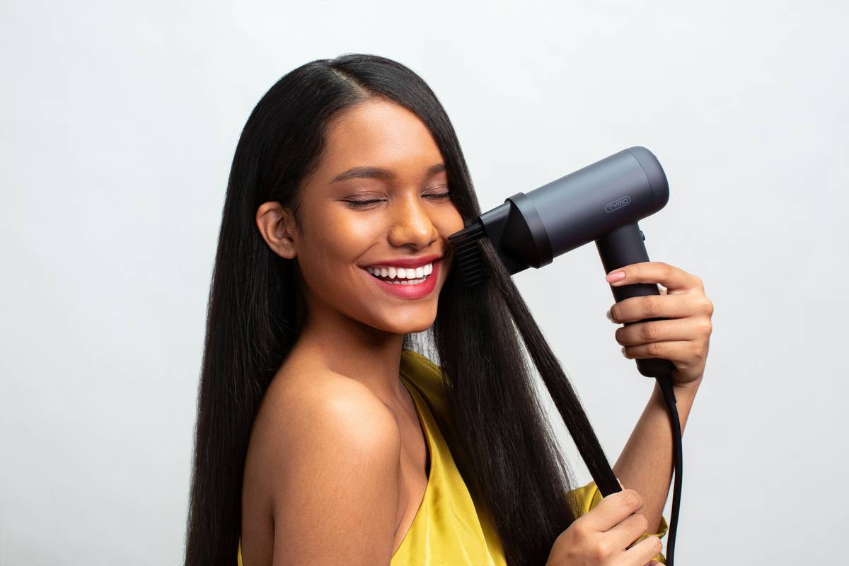Woman using blow dry brushes for women on her arms with warm airflow, standing in bathroom